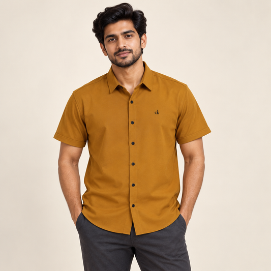Mustard short sleeve pocketless shirt with small black chest embroidery on an adult model